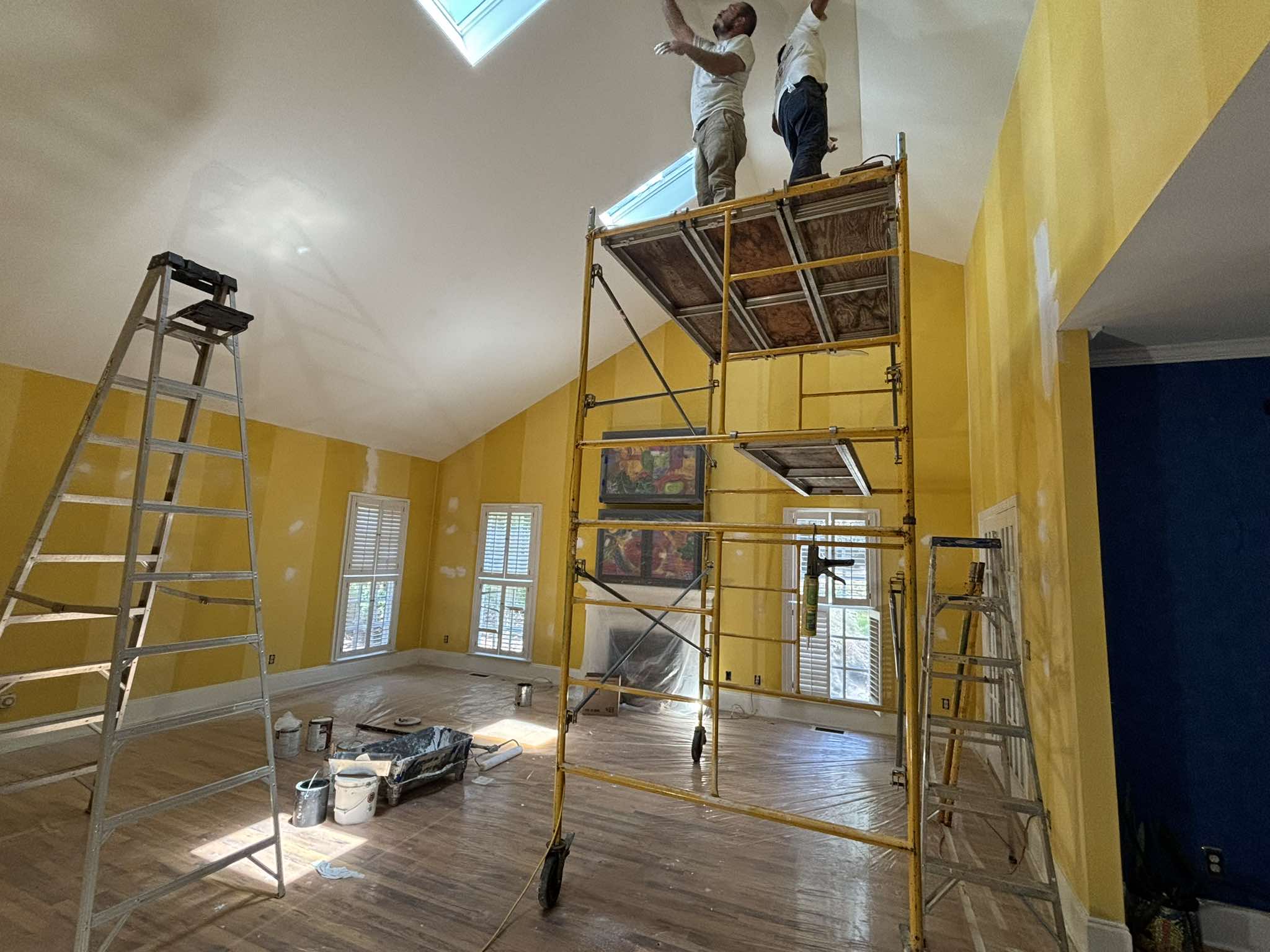 Pintor trabajando desde un andamio cerca de los tragaluces en el interior alto de color amarillo