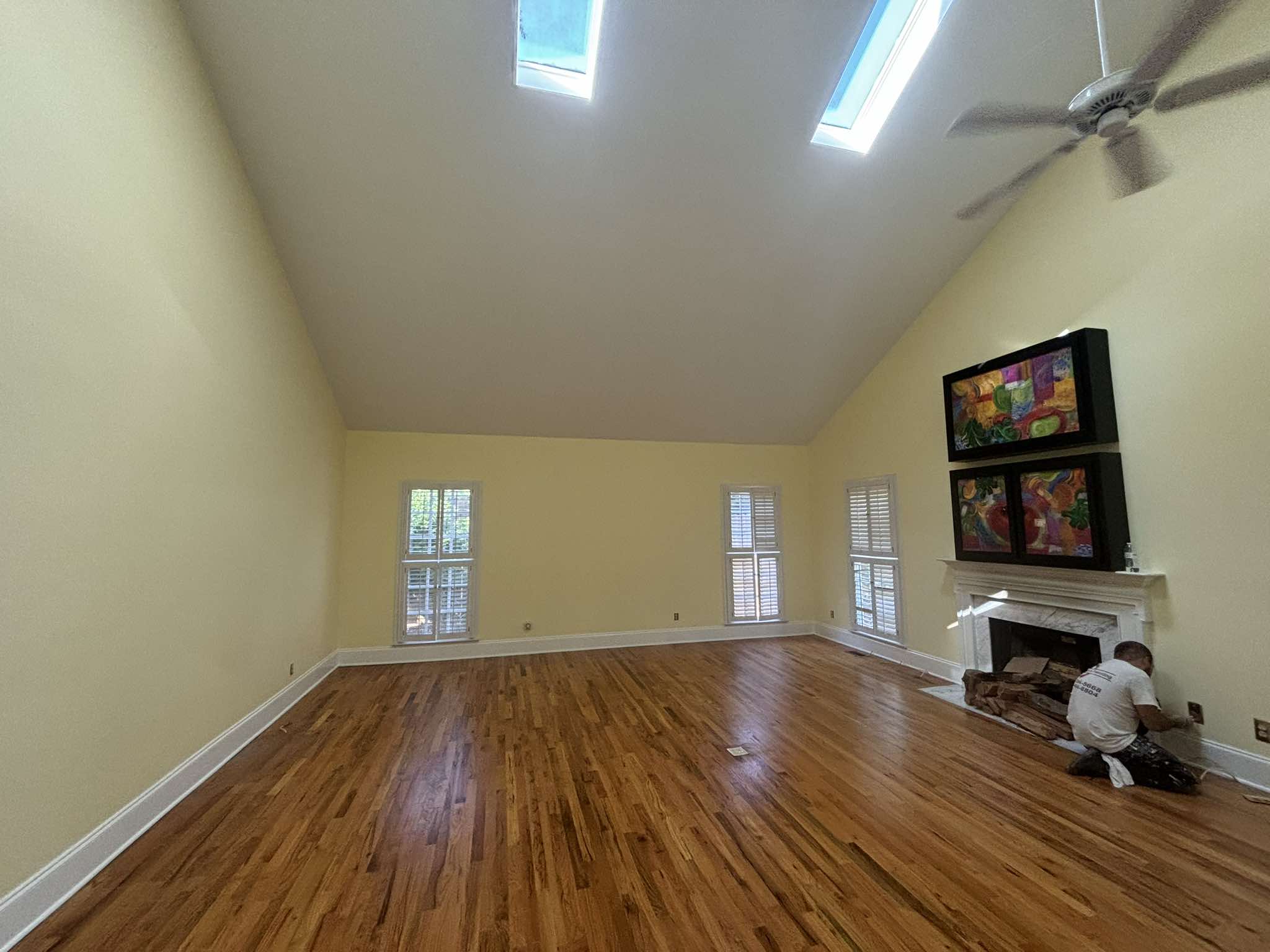 Sala de techo alto terminada con paredes claras, molduras blancas en la chimenea y pisos de madera pulidos